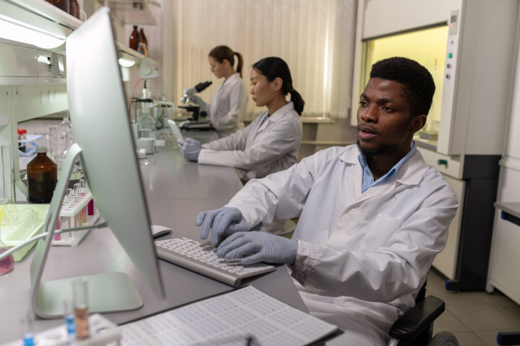 ACADEMY 5 young male scientist gloves whitecoat sitting front computer screen lab