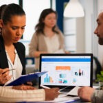 busy multicultural diverse employees analysing annual financial statistics sitting desk front laptop holding documents searching business solutions team businesspeople working company